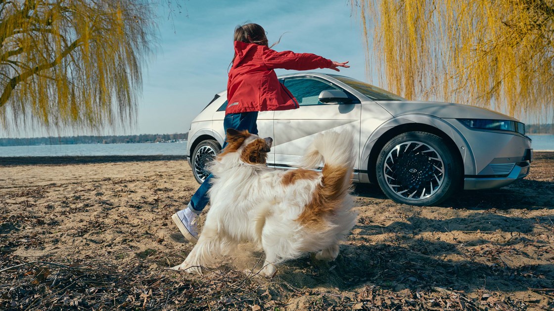 Piger leger med hund på strand foran parkeret Hyundai IONIQ 5